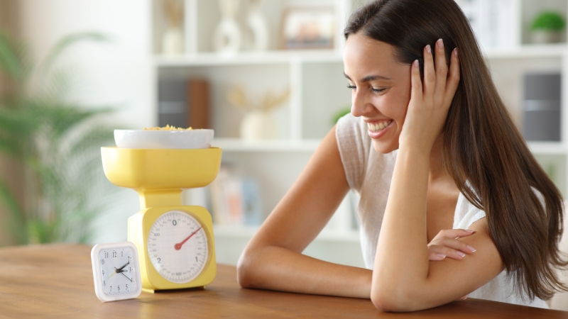 Žena posmatra sat i vagu sa hranom kao simbol fasting dijete i uticaja na metabolizam