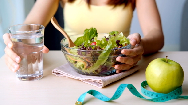Osoba jede salatu uz čašu vode i jabuku kao deo zdravog plana ishrane
