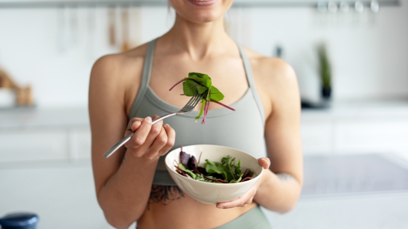 Devojka u sportskoj opremi jede salatu kao obrok posle treninga u kuhinji